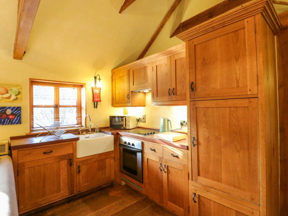 A kitchen with wooden cabinets and appliances at The Old Cow Shed in 