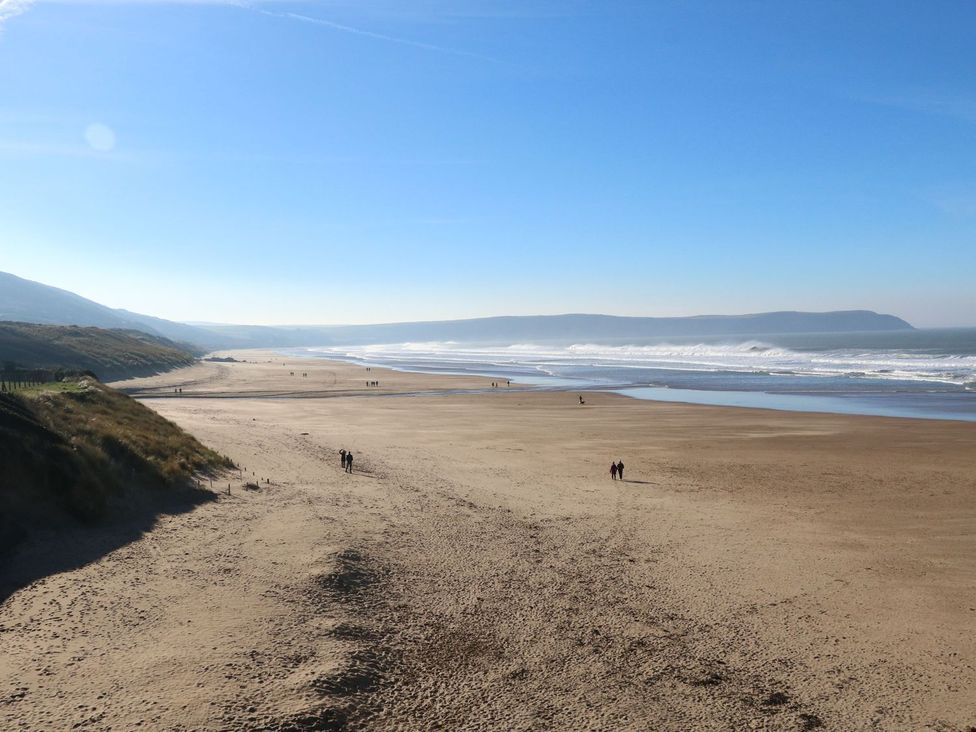 A beach with waves and people walking at Val's Seaview in Ilfracombe