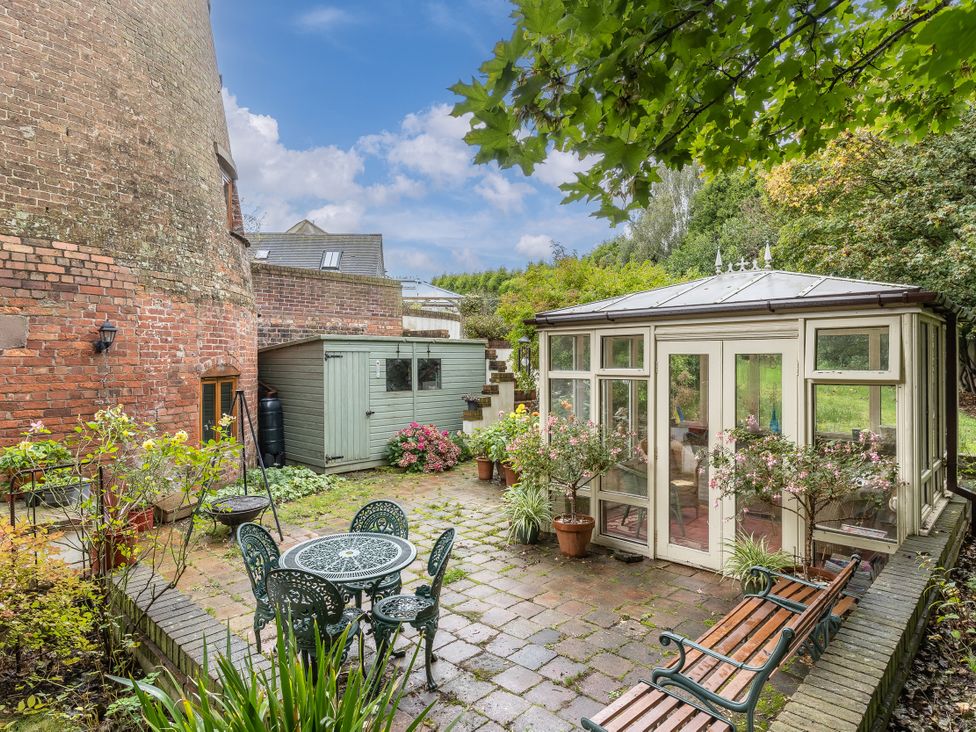 A garden with a greenhouse, table, and chairs at Hadley Park Windmill