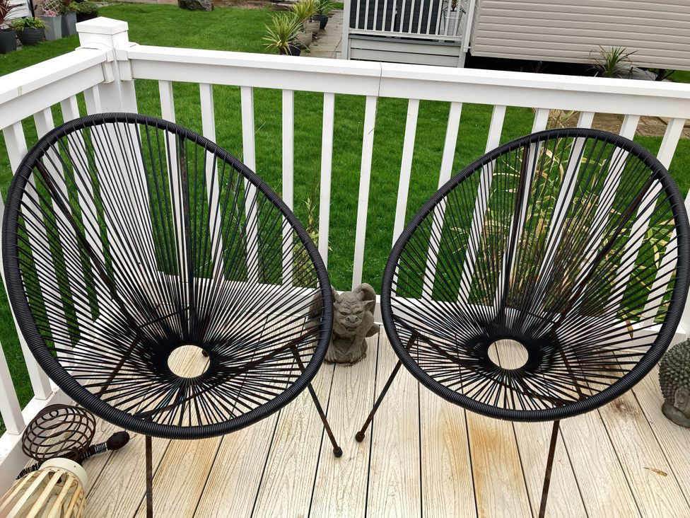 Two black chairs on a deck with a railing at Beachside in Towyn