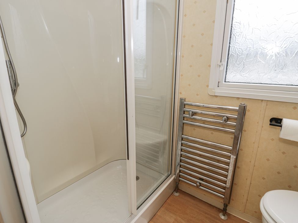 A bathroom with a shower, towel rail, and toilet at Beachside in Towyn