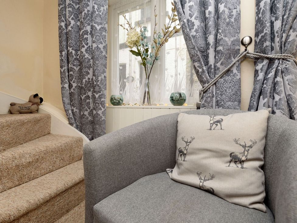 A living area with a staircase and armchair at Dolls Cottage in Looe