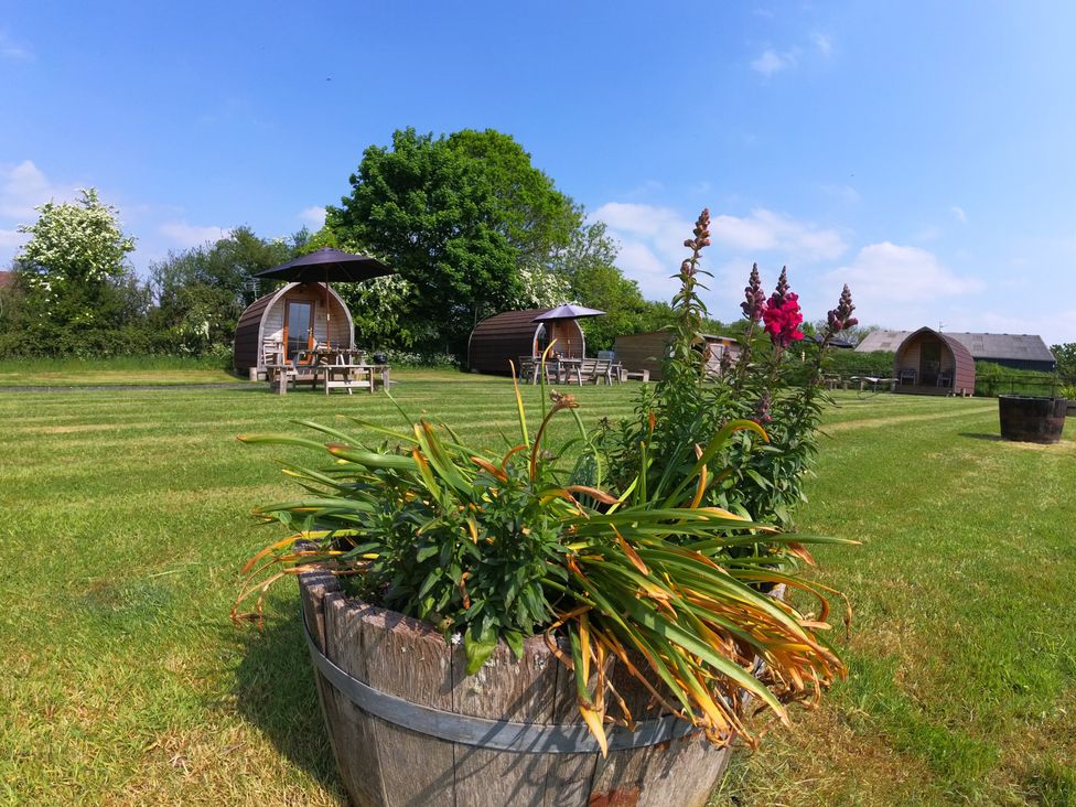Wooden pods with seating area and flowers in barrels at Rosebud Meadow Pod 2 in Malvern