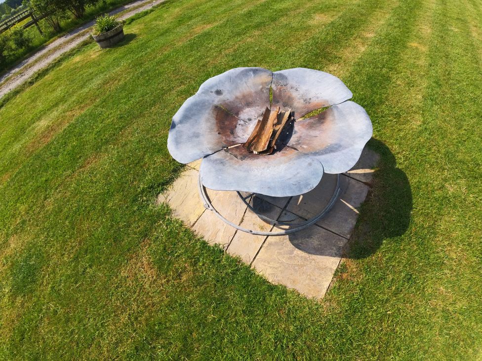 A fire pit with logs on patio stones in a garden at Rosebud Meadow Pod 4 in Malvern