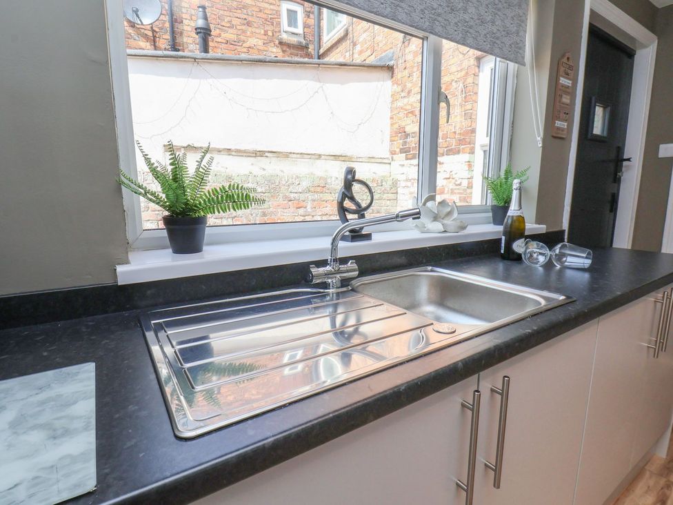A kitchen with a sink, plant, and wine bottle at Crescent Bay House in Filey
