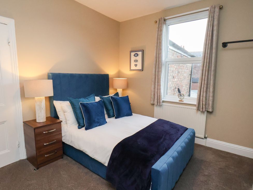 A bedroom with a bed, nightstand, and window at Crescent Bay House in Filey