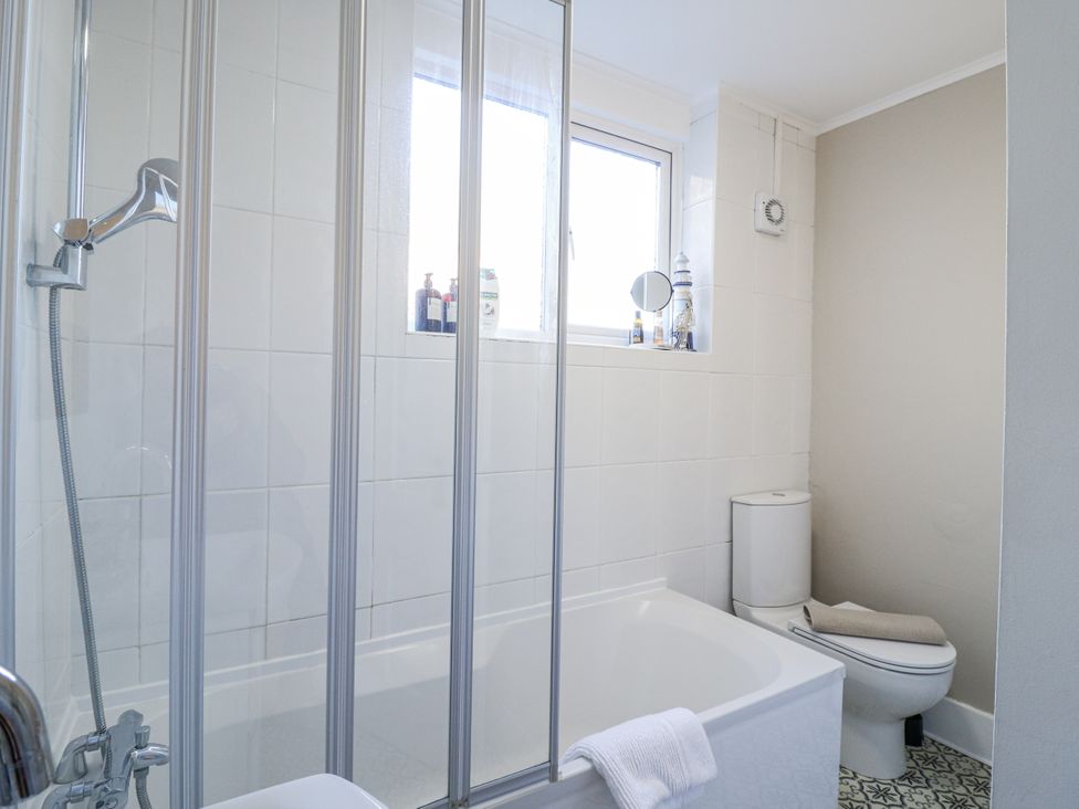 A bathroom with a bathtub, shower, toilet, and window at Beachside Terrace in Harwich