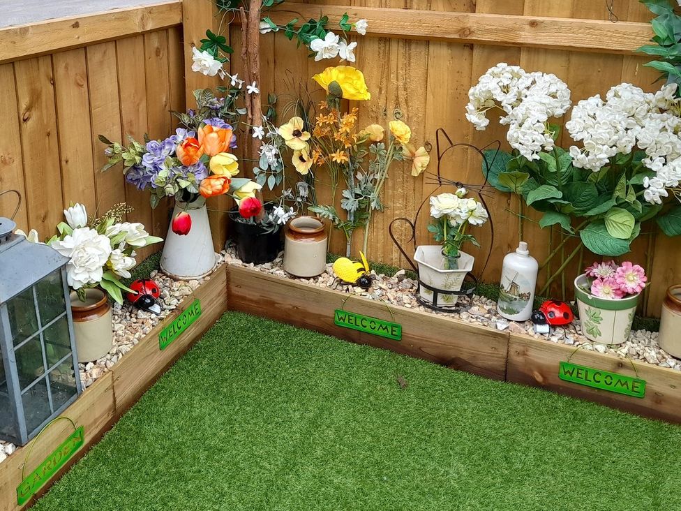 A garden corner with decorative flowers, pots, and a lantern at Greenham Rise Norton-Sub-Hamdon
