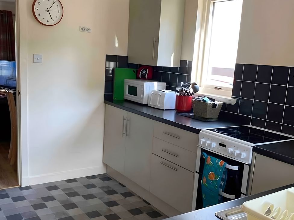 A kitchen with a clock, stove, and microwave at 9 Creag An Iolaire Near Portree