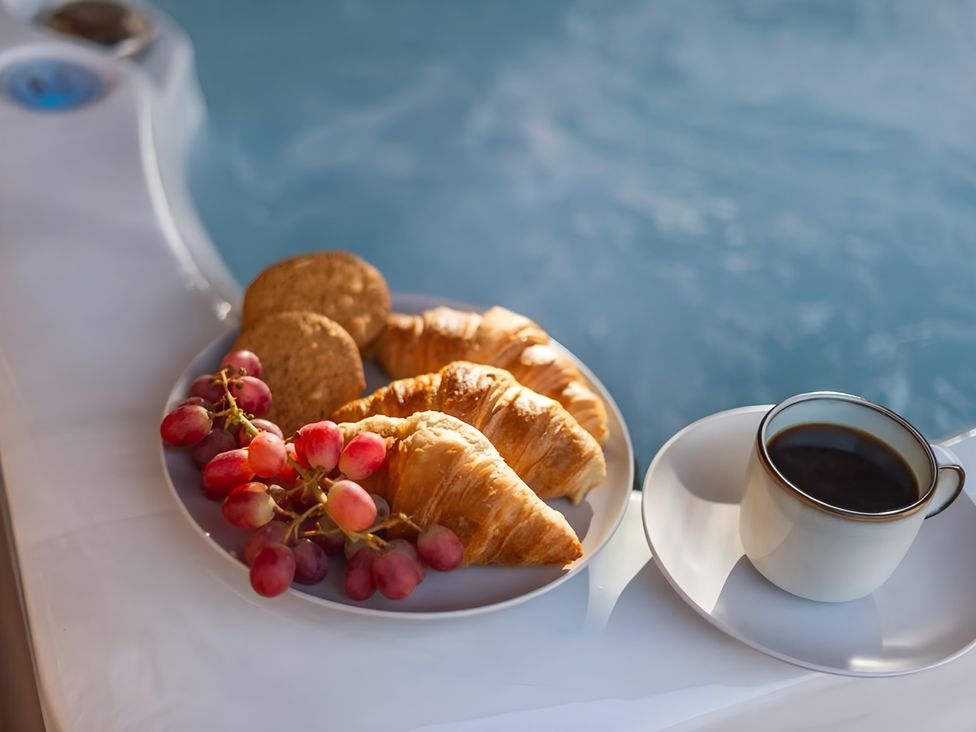 A plate with croissants, cookies, grapes, and a coffee cup by a hot tub