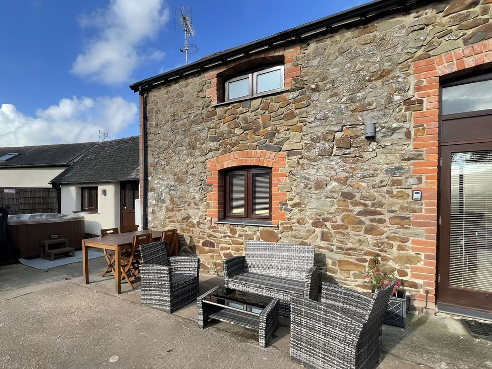 An outdoor seating area with stone wall and hot tub at Granary Barn in Winkleigh