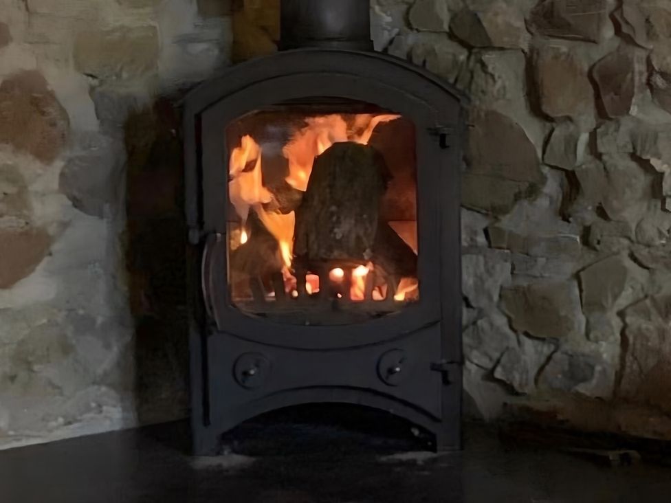 A stove with fire in a living room at Granary Barn in Winkleigh