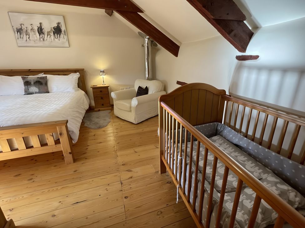 A bedroom with a bed, crib, and sofa at Granary Barn in Winkleigh