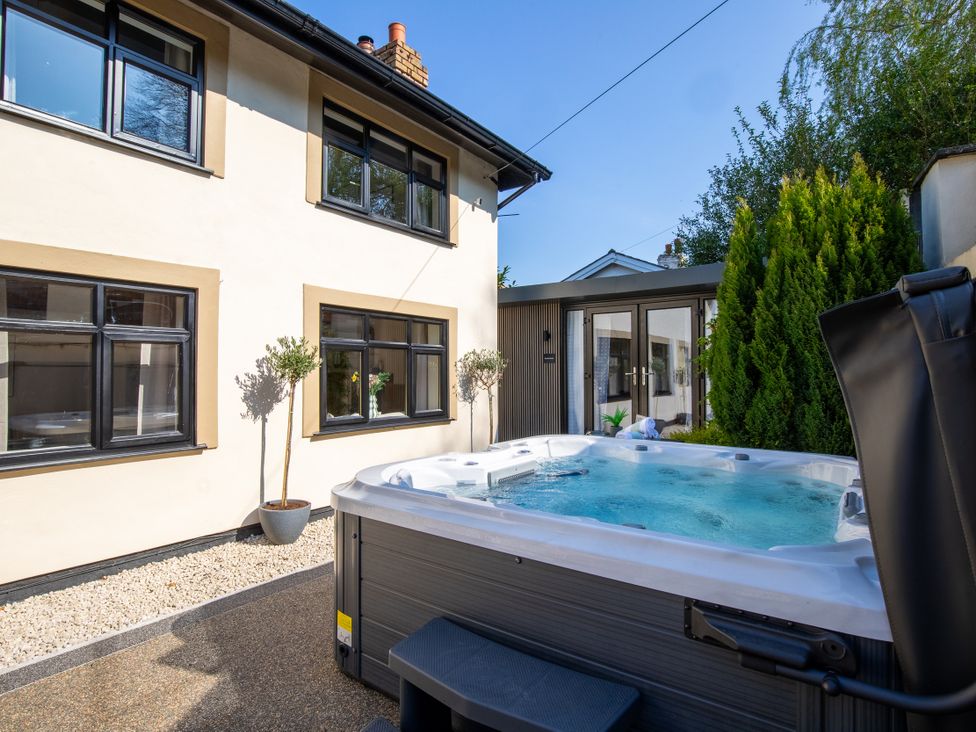 A hot tub on a patio with trees and windows at Rainbow Cottage in Aughton near Ormskirk