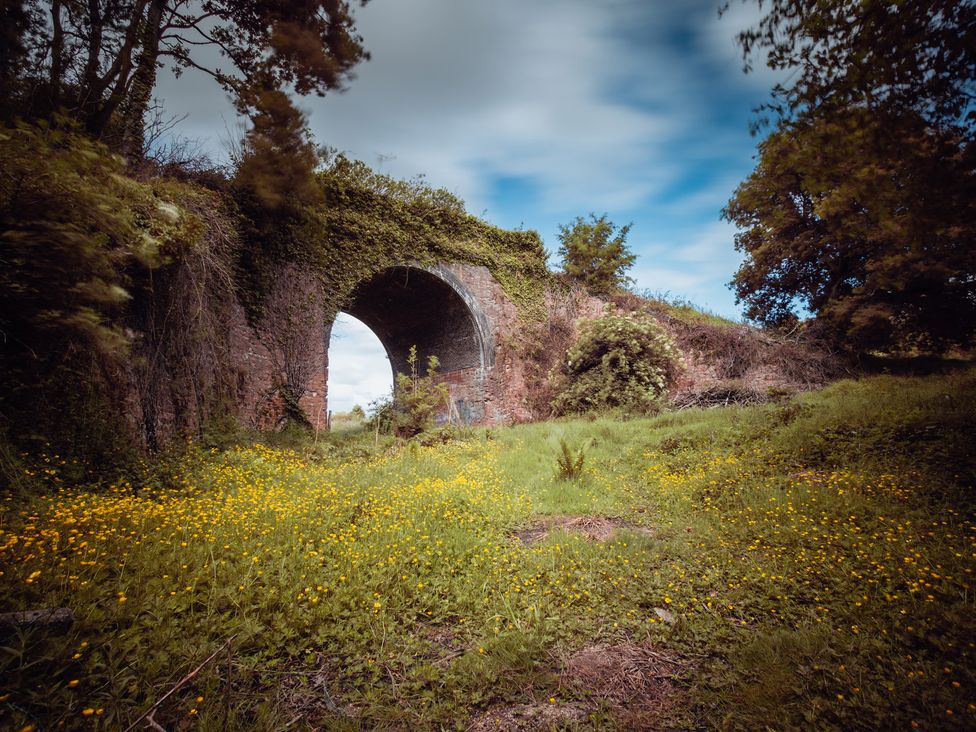 A bridge with an arch surrounded by grass and flowers at Glamping pod-Luxury Glamping Retreat, Battle