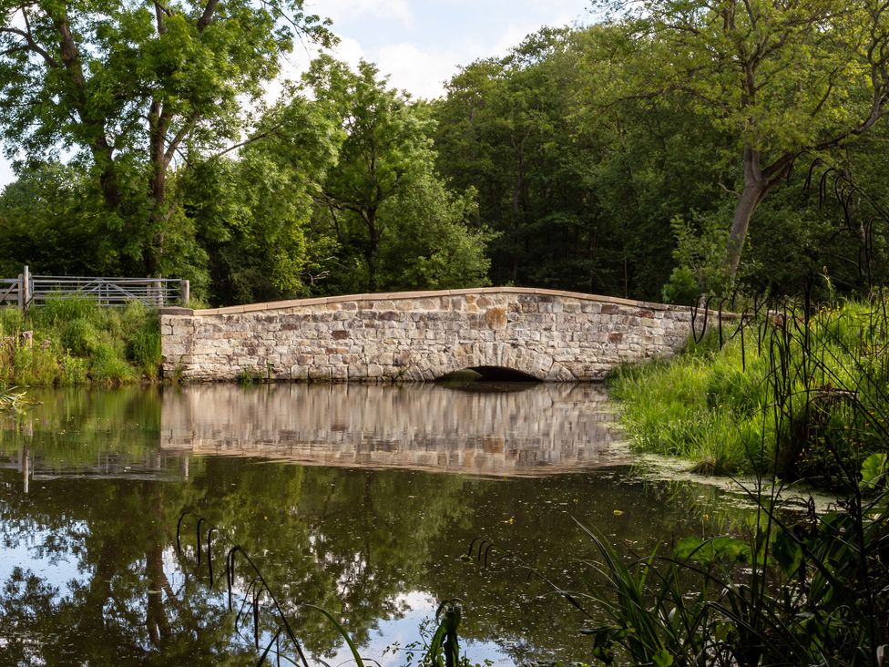 A stone bridge over water with trees and grass at Glamping pod-Luxury Glamping Retreat in Battle