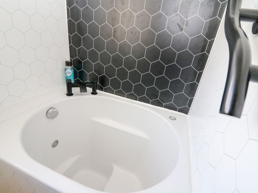 A bathtub with a faucet and black and white tiled wall at Tymelyn in Aberystwyth