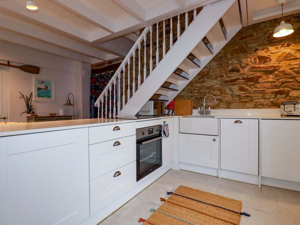 A kitchen with a stove, cabinets, sink, and staircase at Cubbs Corner in Goonbell near St Agnes
