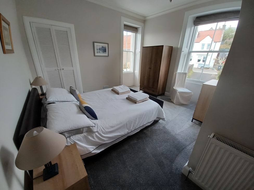 A bedroom with a bed, wardrobe, and bedside lamp at Beach Haven 116 Leven