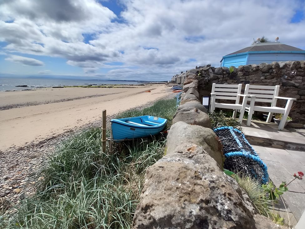 A beach with a blue boat and chairs at Beach Haven 116 in Leven