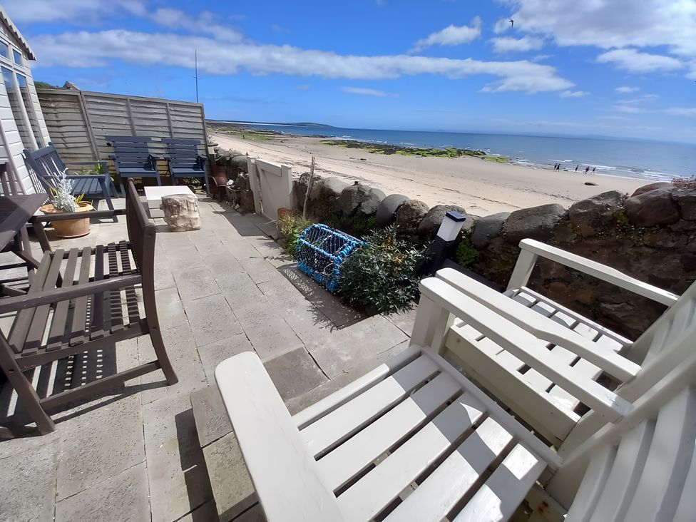 A patio area with chairs and a table overlooking the beach at Beach Haven 116 Leven