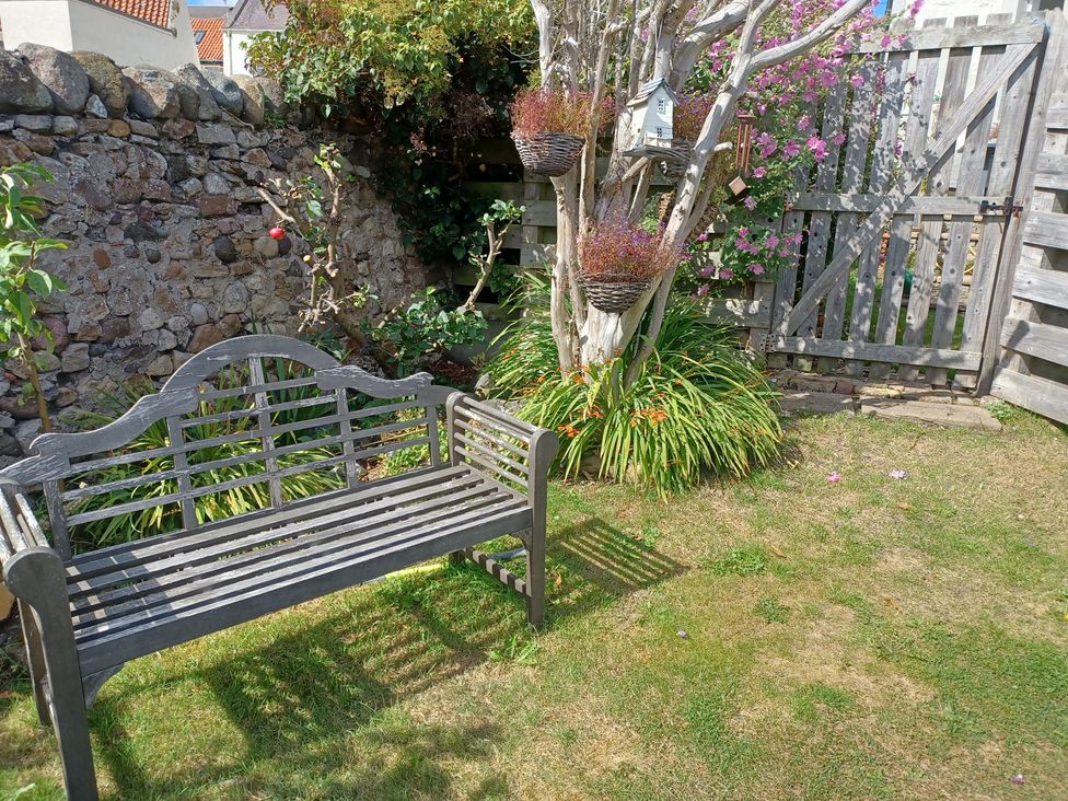 A garden with a bench and flowering plants at Beach Haven 116 in Leven