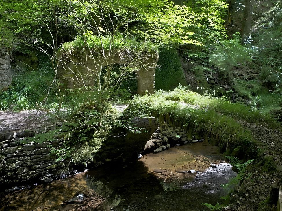 An old stone archway covered in plants near a stream at Satchwell Chalet in Inverness