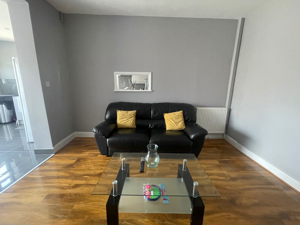 A living room with a black sofa and glass coffee table at Westwick Gardens Retreat in Hounslow