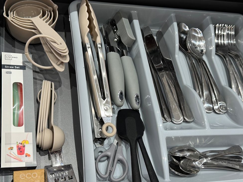 A kitchen drawer containing measuring cups, tongs, a straw set, scissors, and various cutlery at Westwick Gardens Retreat Hounslow