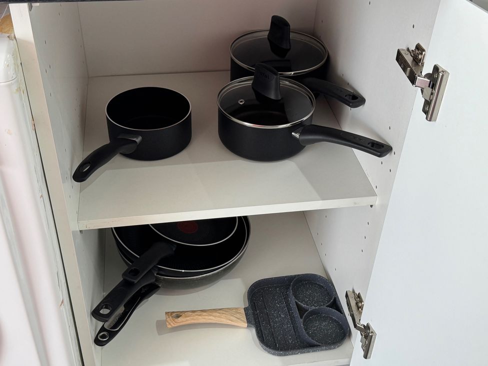 A kitchen cabinet with pots and frying pans at Westwick Gardens Retreat Hounslow