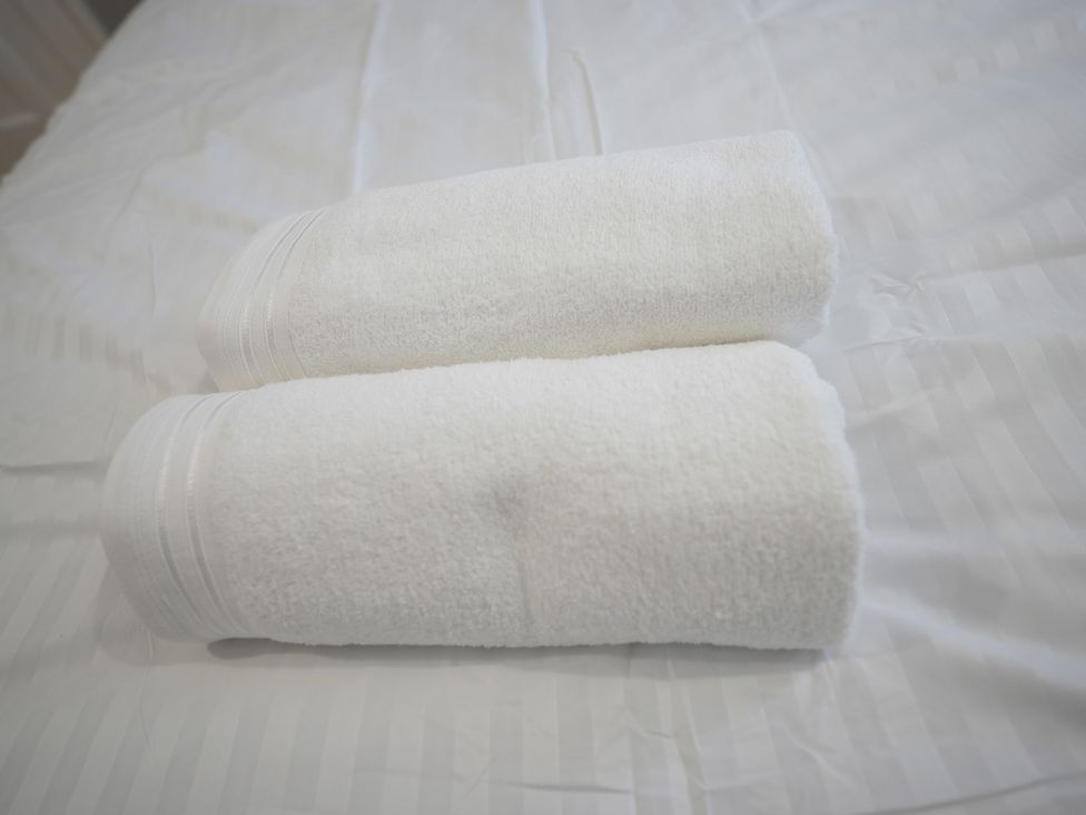 Two rolled white towels on a bed at Westwick Gardens Retreat in Hounslow