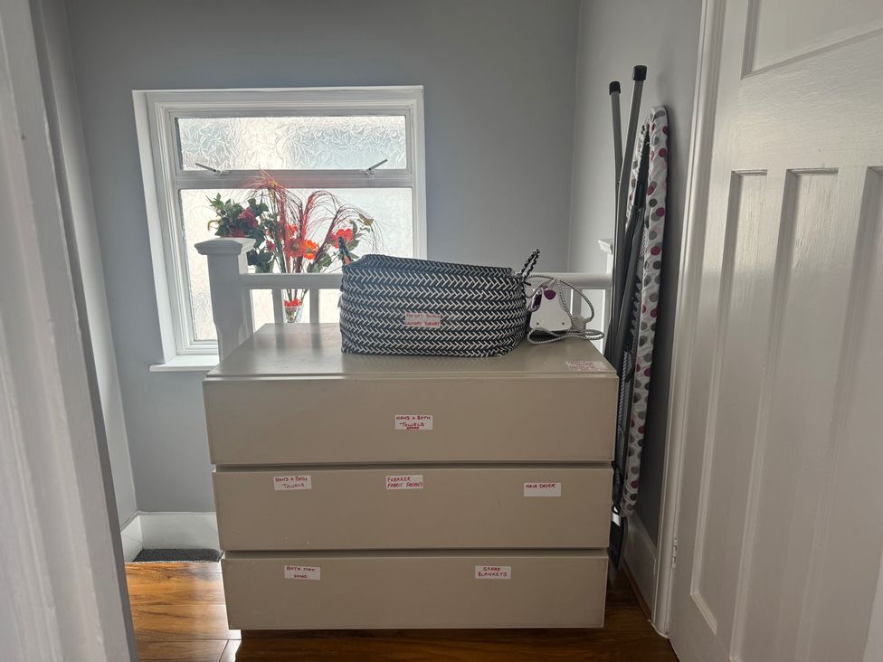 A dresser with storage bins and an ironing board in a hallway at Westwick Gardens Retreat Hounslow