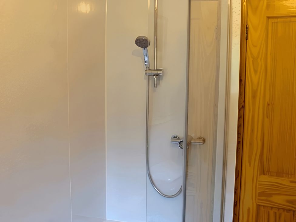 A shower with a chrome showerhead and glass door at Culnacraig in Stranraer