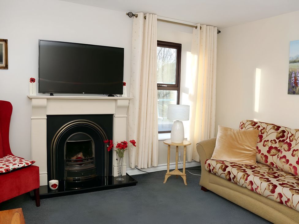 A living room with a television, fireplace, sofa, and armchair at The Farmhouse in Omagh
