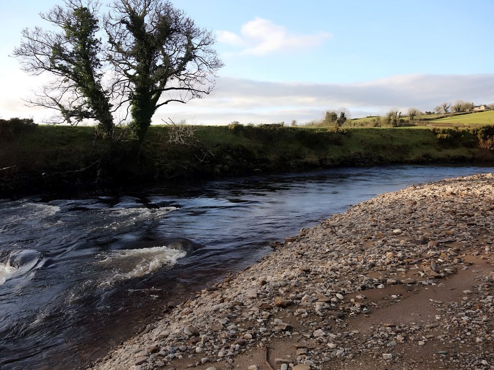 A river with trees on the bank and pebbles at The Farmhouse in Omagh