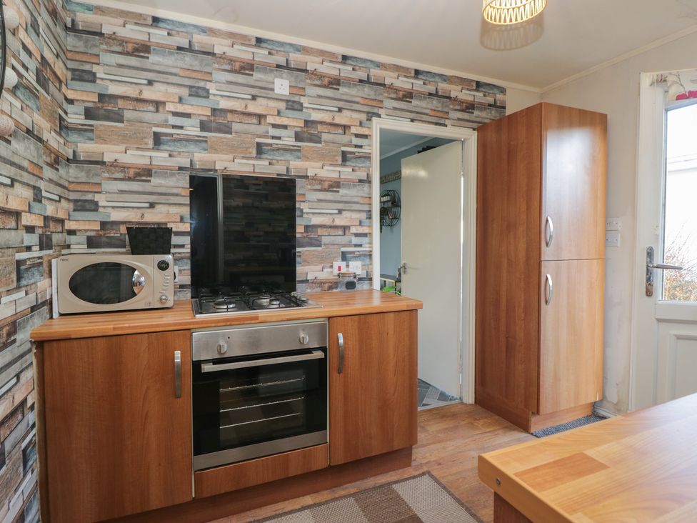 A kitchen with a microwave, gas stove, and wooden cabinets at Beechtree Lodge 57 Denny