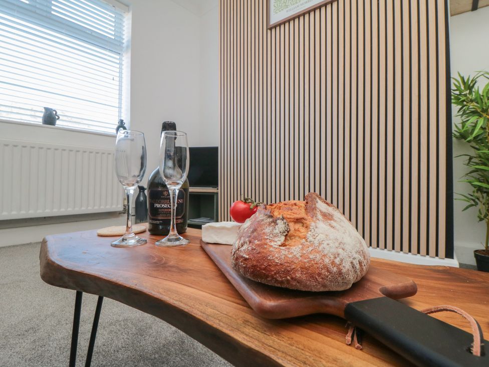A living room with a wooden table, glasses, bottle, bread, and tomato at Isla’s Sea Forge in Skinningrove