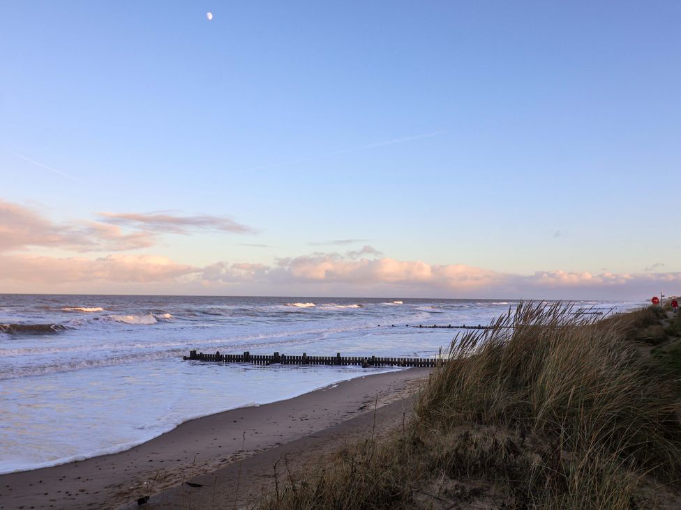 A beach with waves and grass near the shore at Paws By The Sea in Norwich
