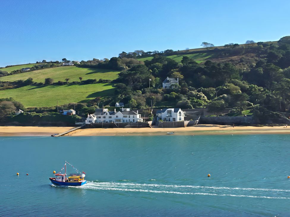A beach with a boat on the water and houses on a hill at Villa 8, Estura in Salcombe