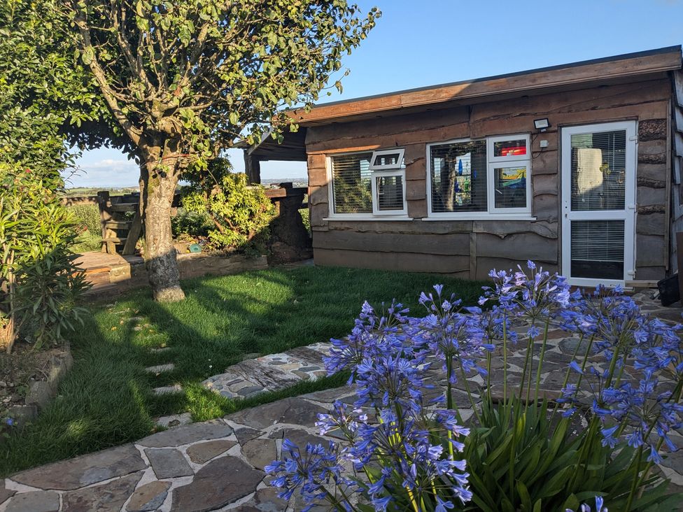 An outdoor area with a cabin, pathway, and flowers at The Retreat Cabin in Llanelli