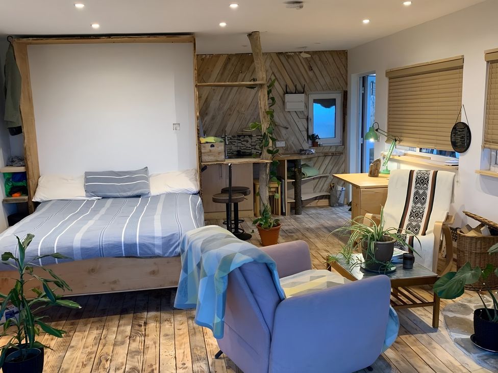 A studio with a bed, couch, table and shelves at The Retreat Cabin in Llanelli