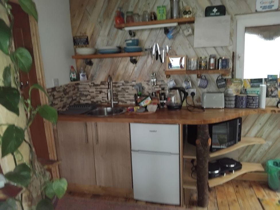 A kitchen with a sink, fridge, microwave, and shelves at The Retreat Cabin in Llanelli