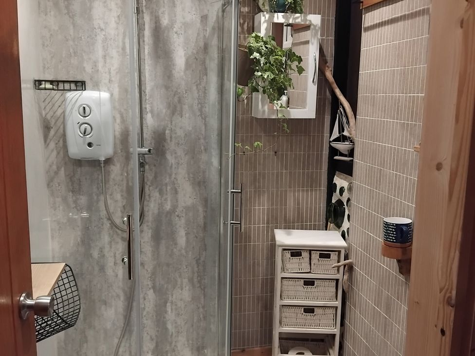 A shower with wall panels and storage basket at The Retreat Cabin in Llanelli