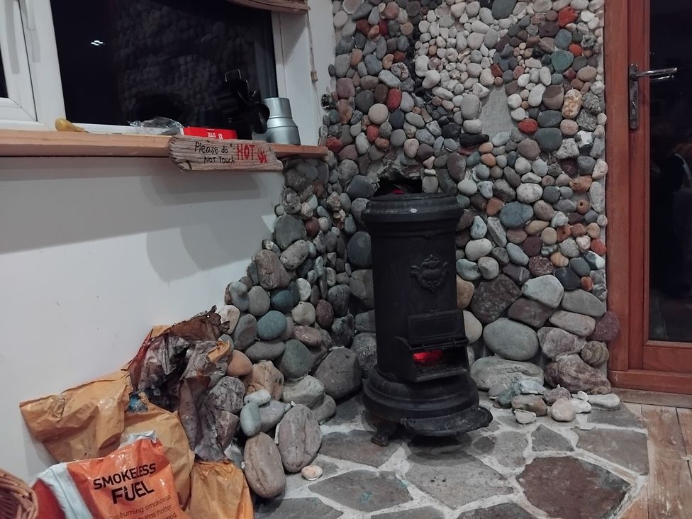 A living room featuring a wood stove and stone wall at The Retreat Cabin in Llanelli