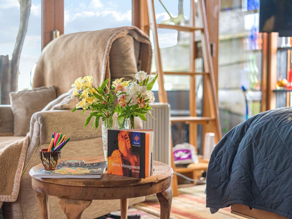 A living room with a flower vase and books on a table at The Retreat Cabin in Llanelli