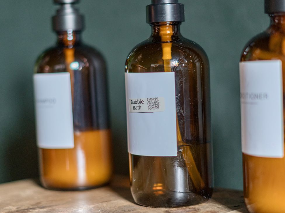 A bathroom with shampoo, conditioner, and bubble bath bottles on a wooden surface at Coach Lodge, Retford