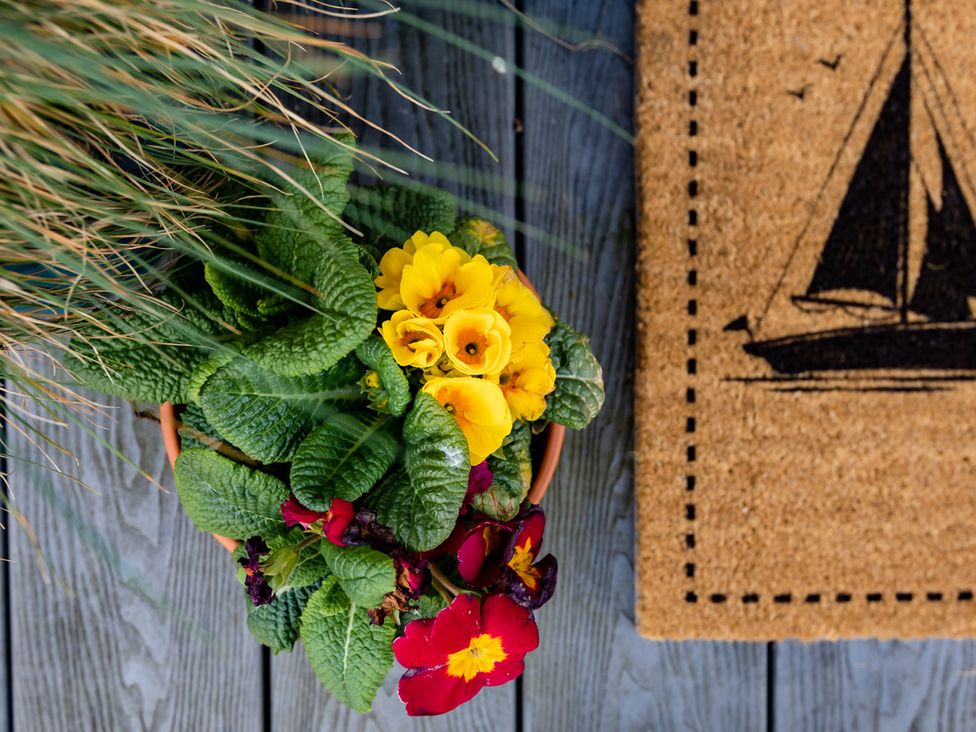 A flower pot with yellow and red flowers next to a welcome mat at 11A Cards Wynd Anstruther