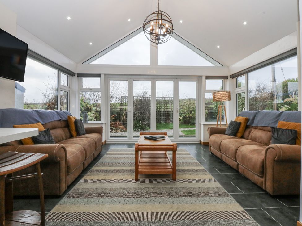 A conservatory with sofas and a table at Benlli in Pwllheli