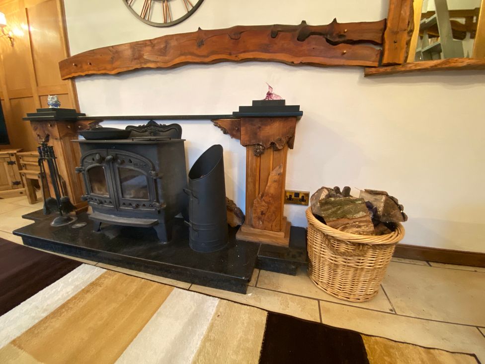 A fireplace with a wood stove and log basket at Whispering Trees Cottage in Thornhill