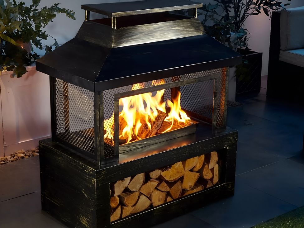 A fireplace with logs and fire at Whispering Trees Cottage Thornhill